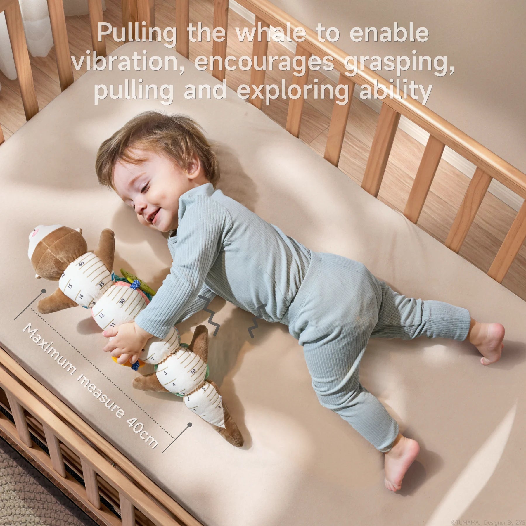 A smiling baby in light blue ribbed pajamas lies on a cream-colored crib mattress, hugging the soft otter sensory toy that doubles as a measuring tool. The toy is stretched out alongside the baby, showing its full length with measurement indicators clearly visible on the underside. The plush toy features a brown otter head at one end and colorful segments between, with measurement markings ranging up to 40cm as indicated by text at the bottom of the image. The blue whale teether is visible with a zigzag lin