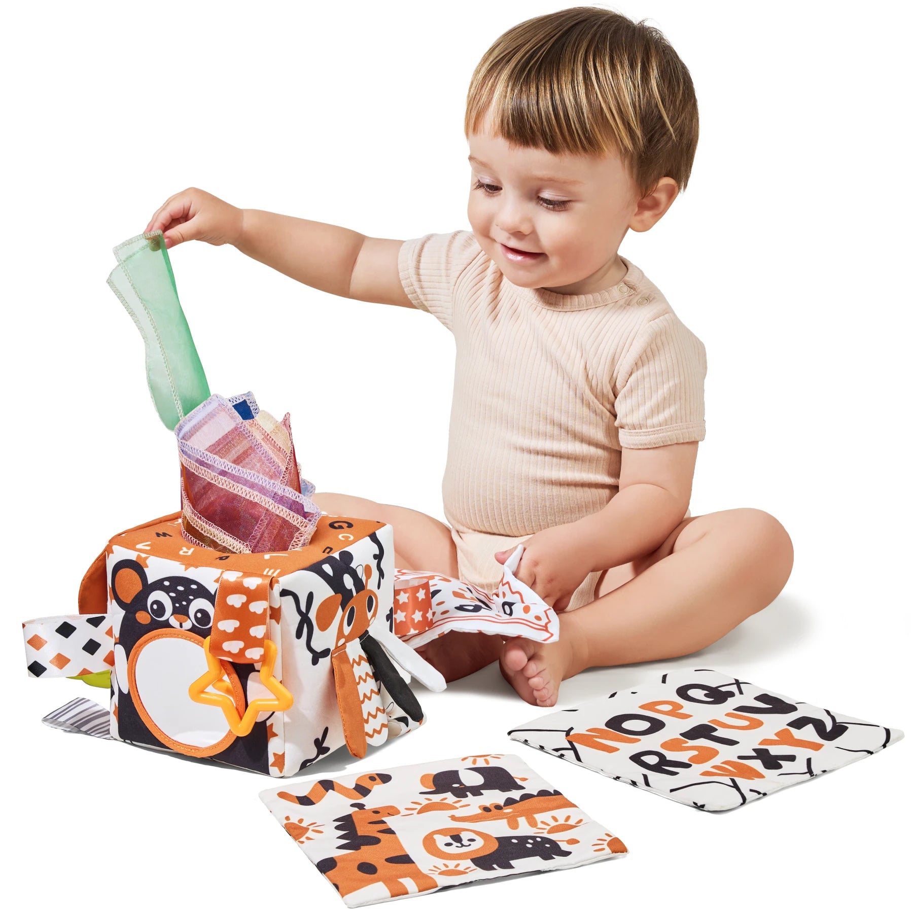 Baby sitting on the floor playing with sensory tissue box toy, fabric books, and alphabet cards for early learning and cognitive development