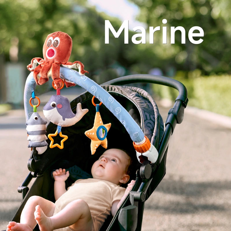 A baby lying in a stroller, gazing up at a marine-themed arch toy featuring a plush octopus, whale, starfish, and striped fish. The toy is securely attached to the stroller, providing sensory and interactive play on the go.