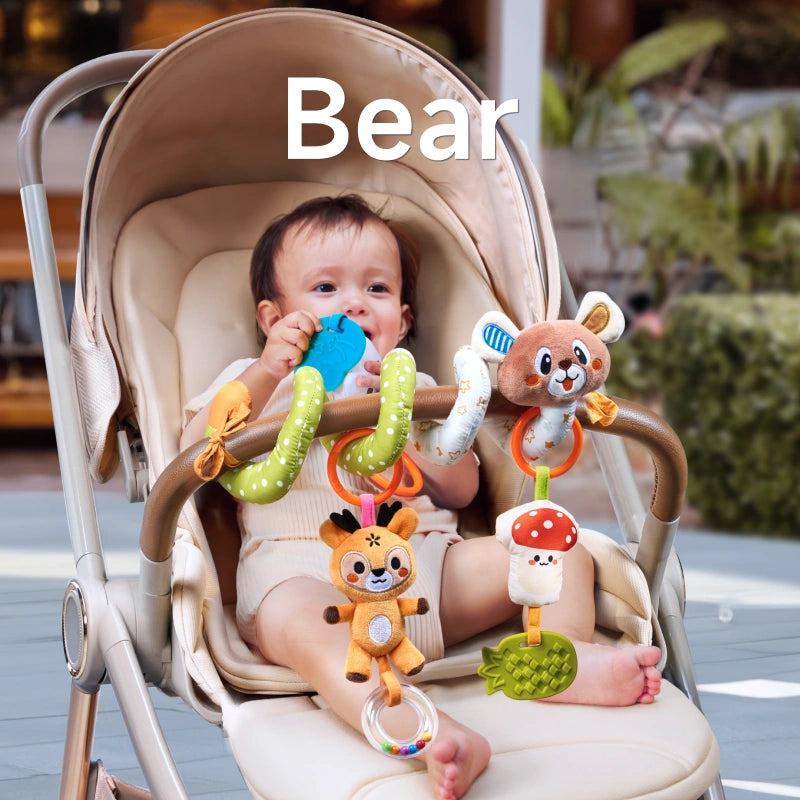 A baby sitting in a stroller, playing with a bear-themed spiral toy. The toy features a plush bear, deer, mushroom, pineapple teether, and bead rattle, securely attached to the stroller for engaging playtime.