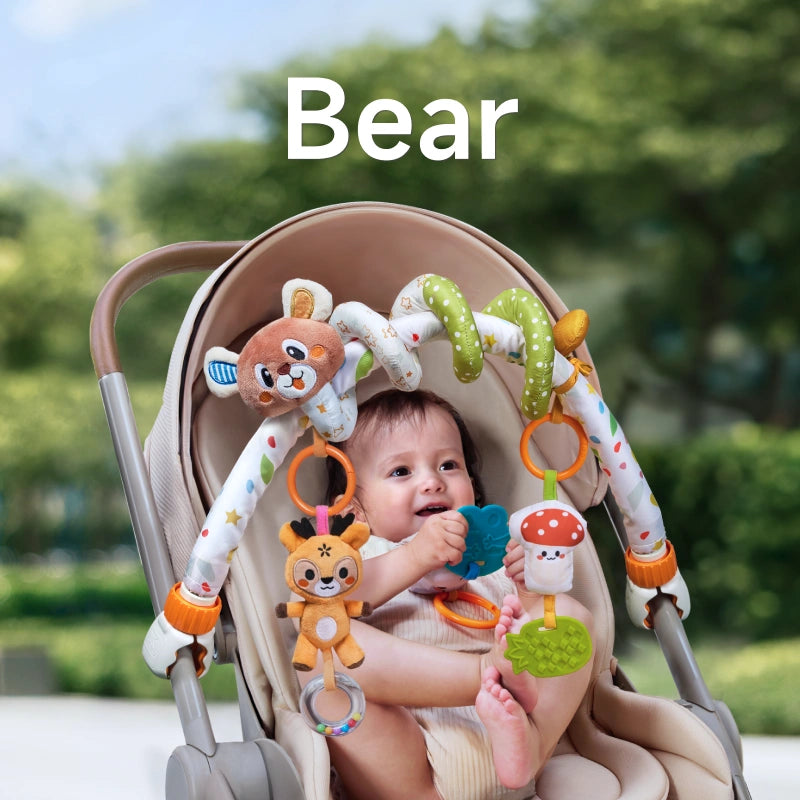 A baby sitting in a stroller, smiling and playing with a bear-themed arch toy. The toy features a plush bear, deer, mushroom, pineapple teether, and bead rattle, securely attached to the stroller for interactive fun.