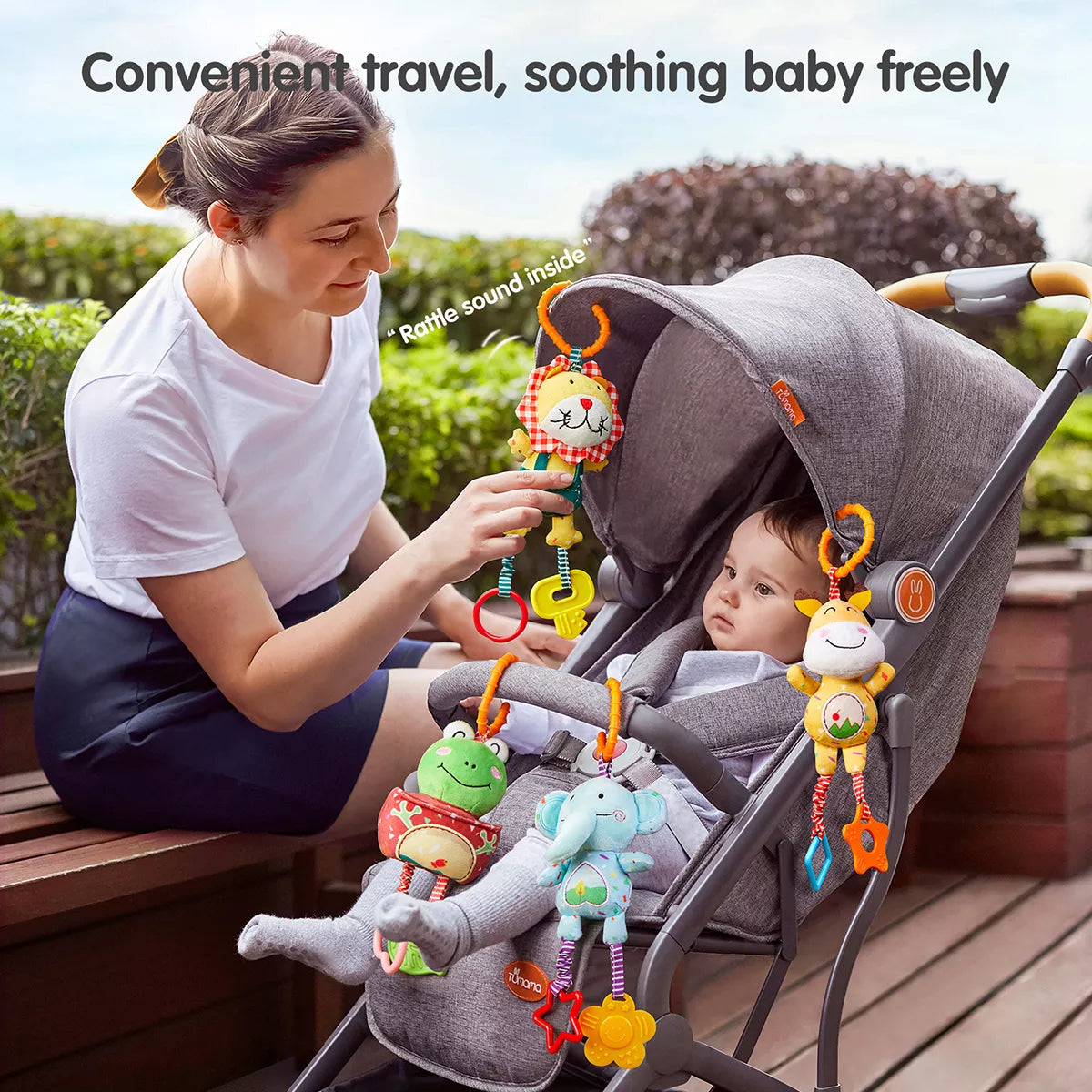 A mom pushing a stroller with a frog deer elephant lion toy hanging from it